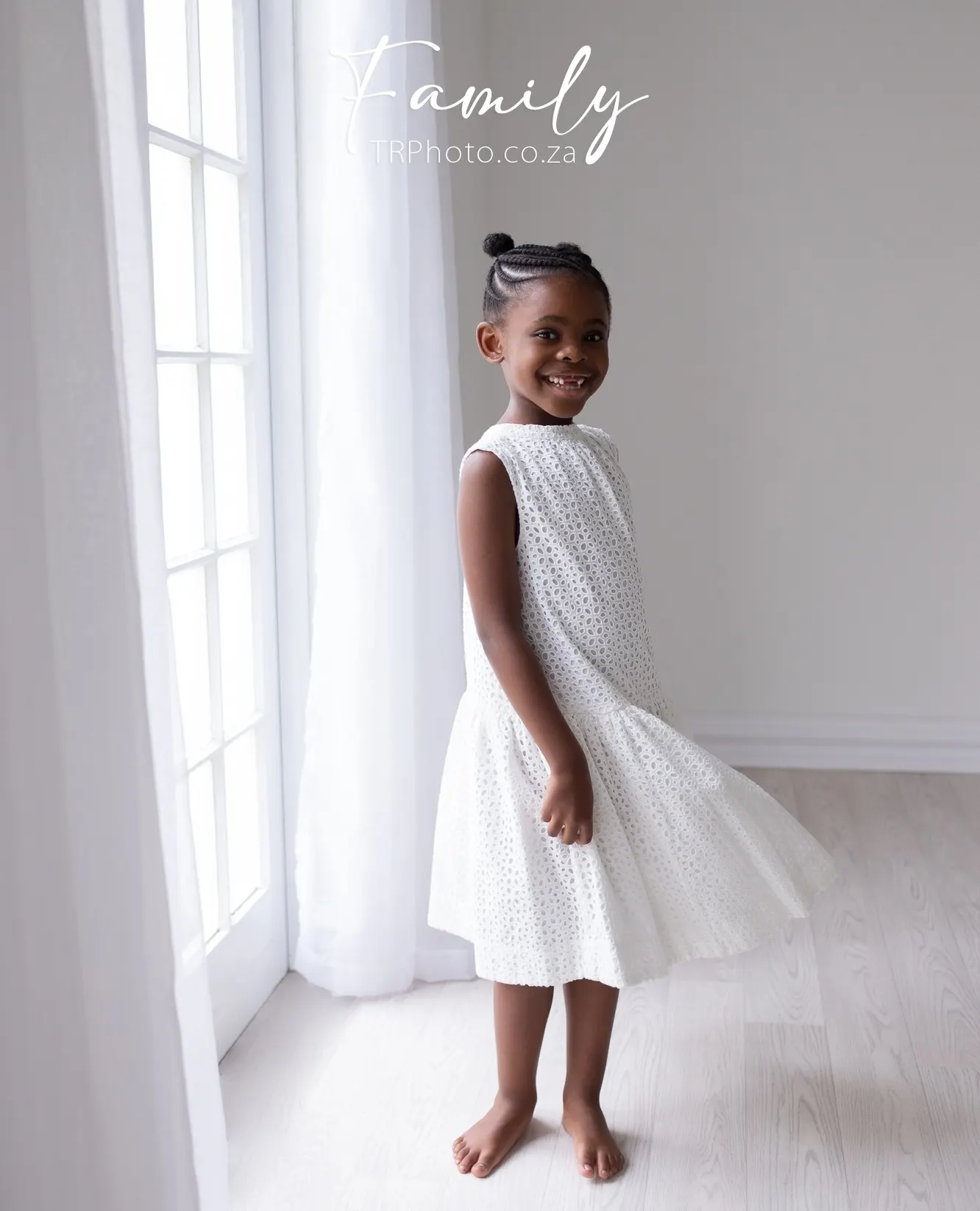A little girl in a white dress by a window