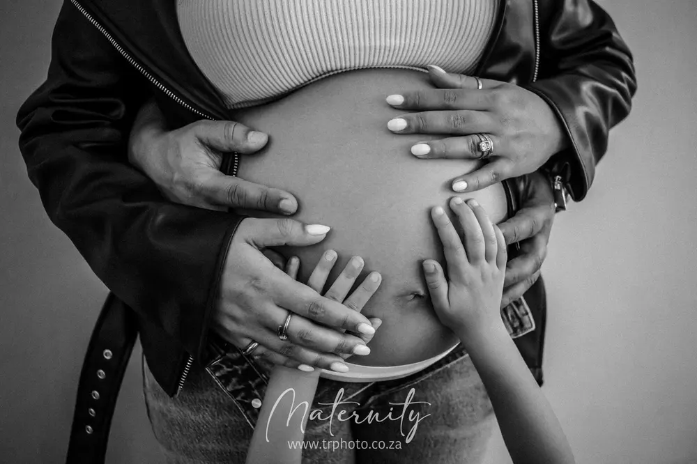 A family's hands resting on a pregnant belly