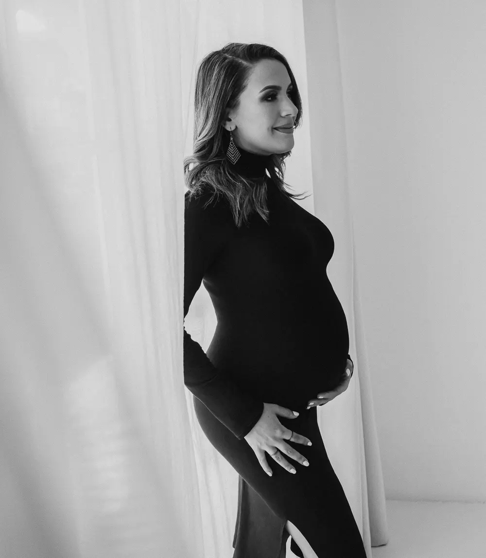 An expecting mother in a black dress by a window