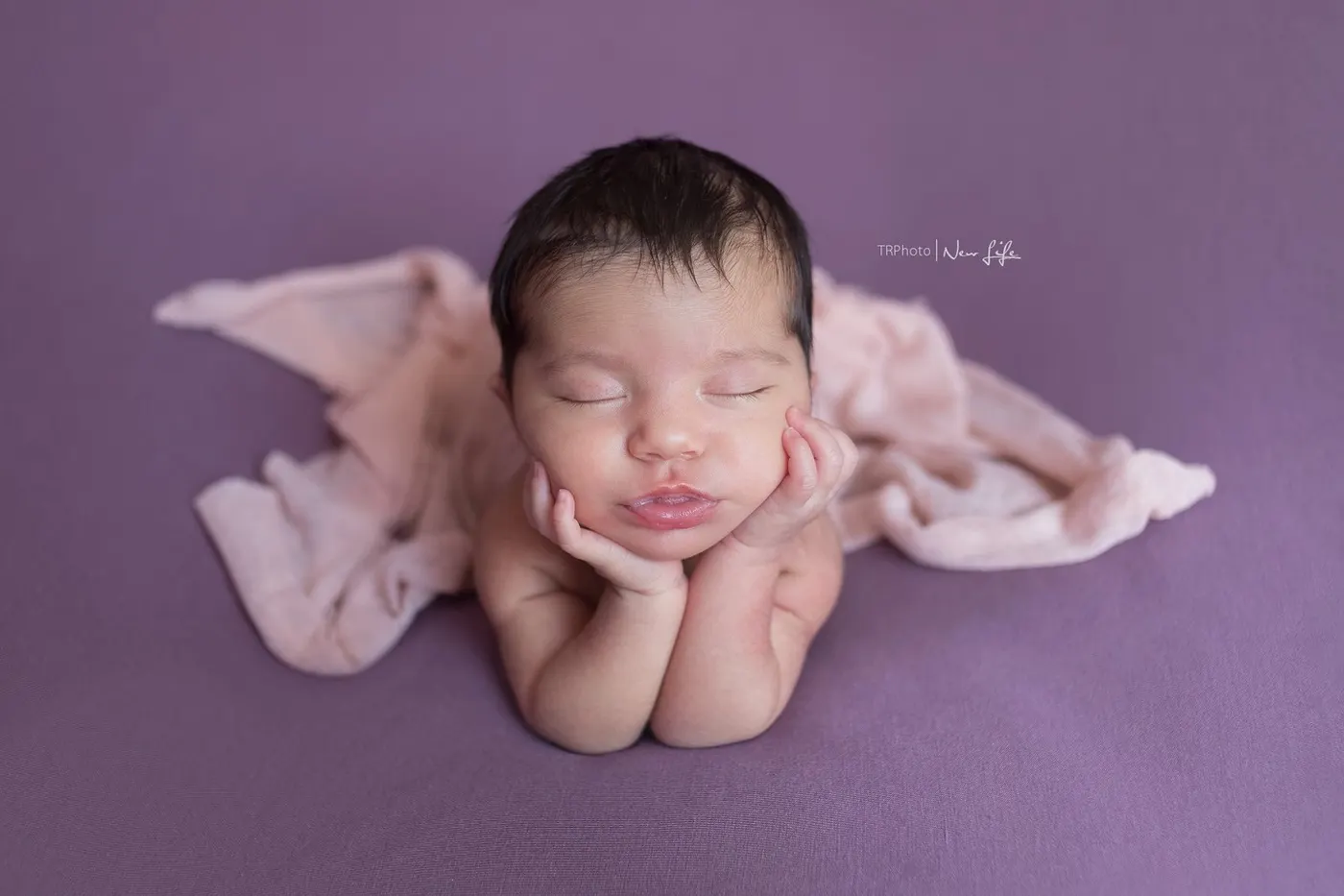 A sleeping newborn posed on a purple blanket